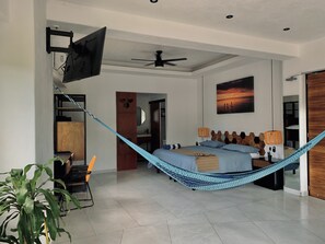 A modern bedroom with a bed, a hammock, a ceiling fan, and a wall-mounted TV. - Casa Makawe - Adults Only (Sayulita)