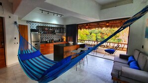 Una cocina moderna con una isla central, un comedor con una hamaca y un balcón con vistas a zonas verdes.