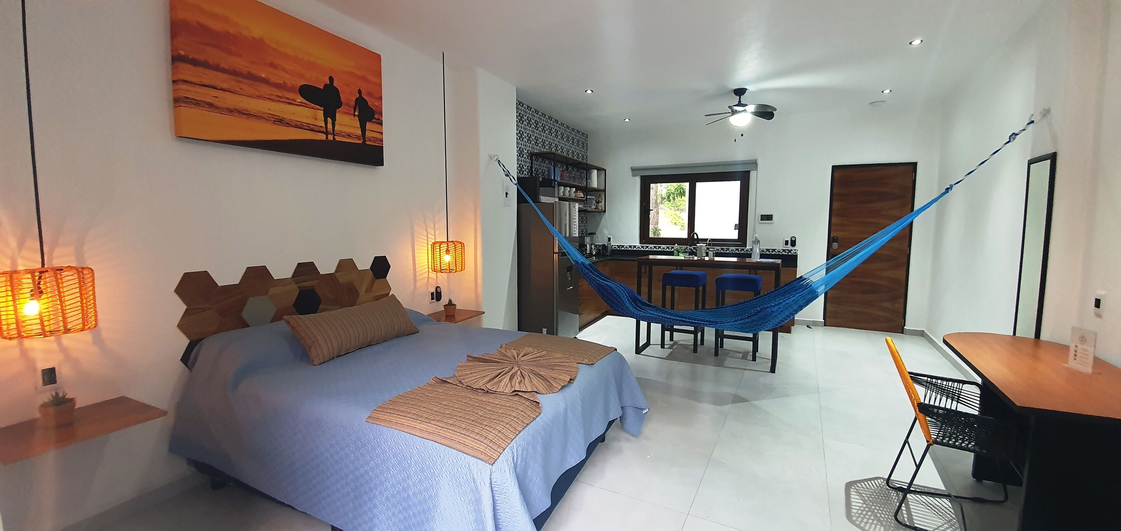 Ein Schlafzimmer mit einem Bett, Nachttischlampen, einer Hängematte, einem Schreibtisch und einem Fenster.