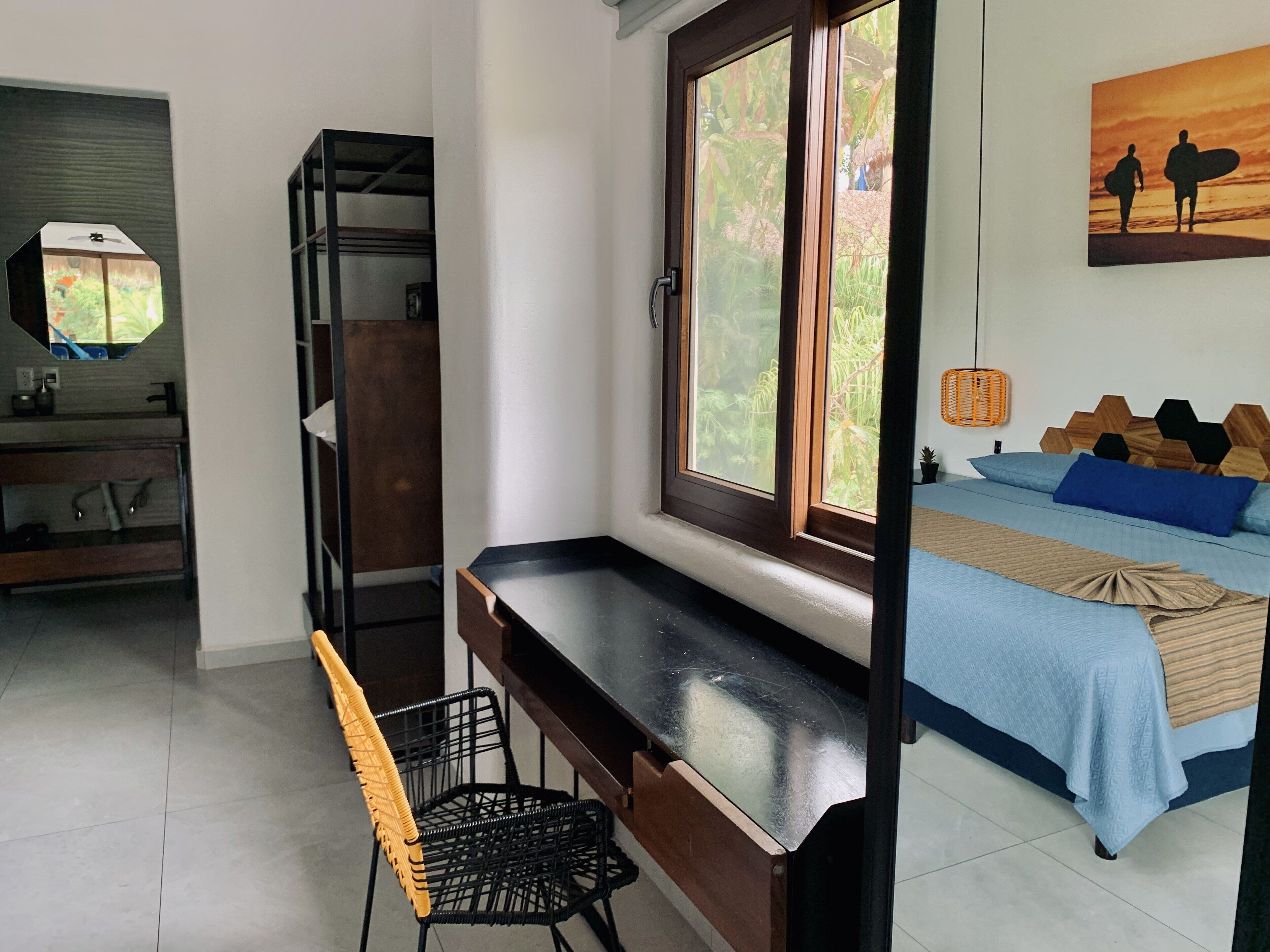 Une chambre à coucher avec un lit, un bureau, une chaise, une fenêtre et un tableau accroché au mur.