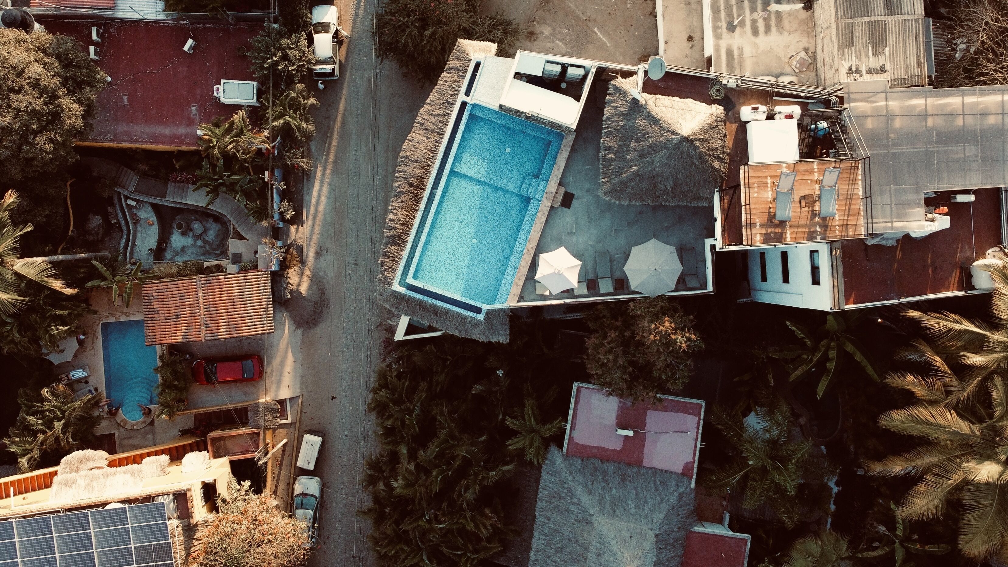 An aerial view of a property with a rectangular swimming pool, adjacent to a building with a flat roof and a covered patio area.