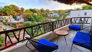 Un balcón con dos sillas azules acolchadas y una mesita pequeña, con vistas a una zona residencial con edificios y vegetación.