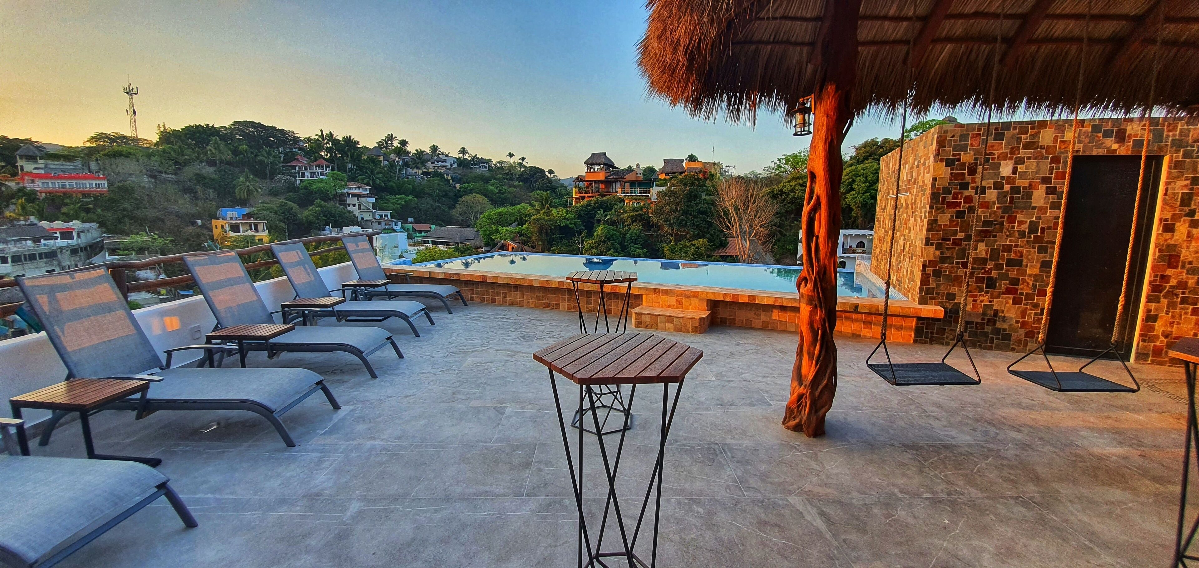 A rooftop terrace with a swimming pool, lounge chairs, and a thatched-roof structure.