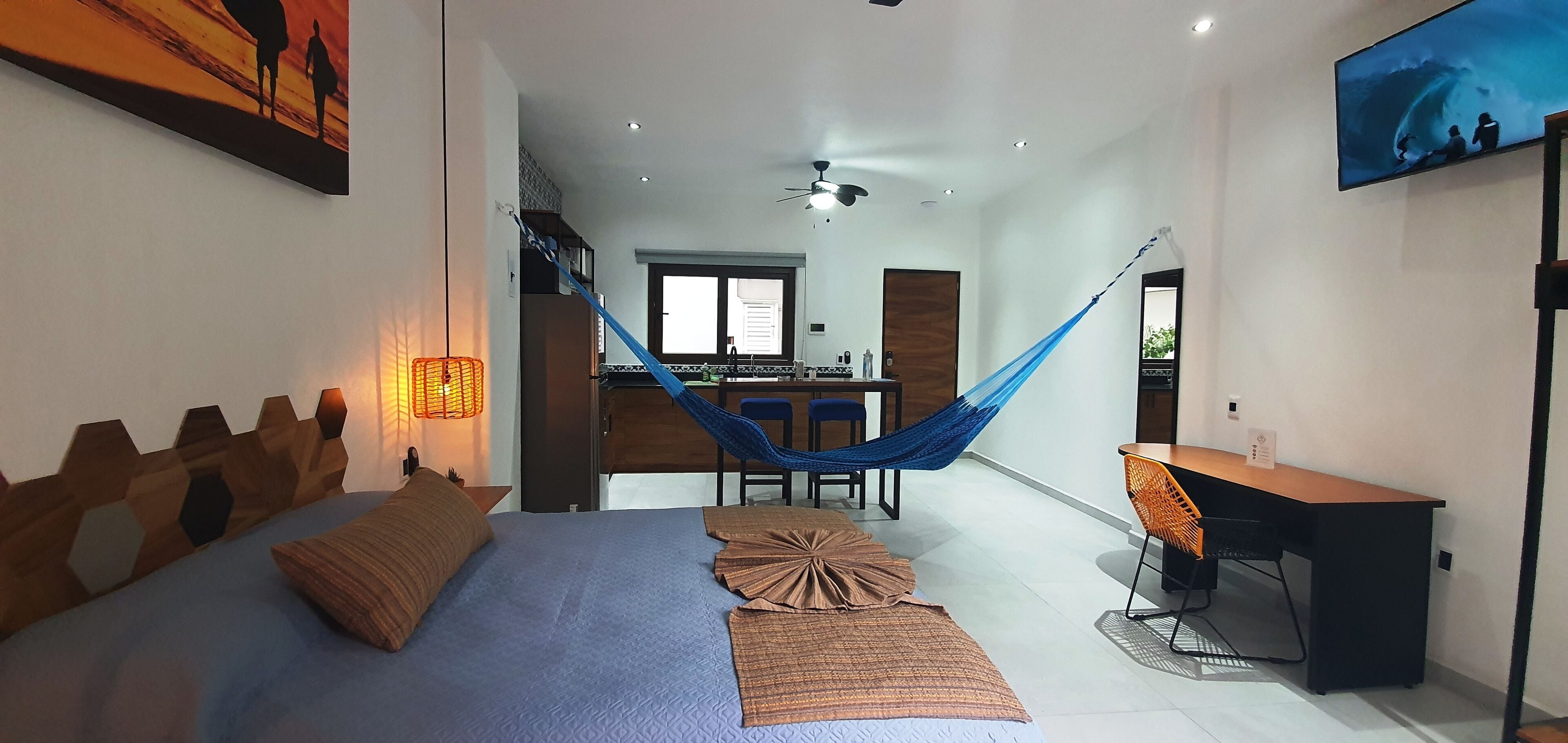 A modern hotel room with a bed, a desk, a chair, a hammock, and a TV.