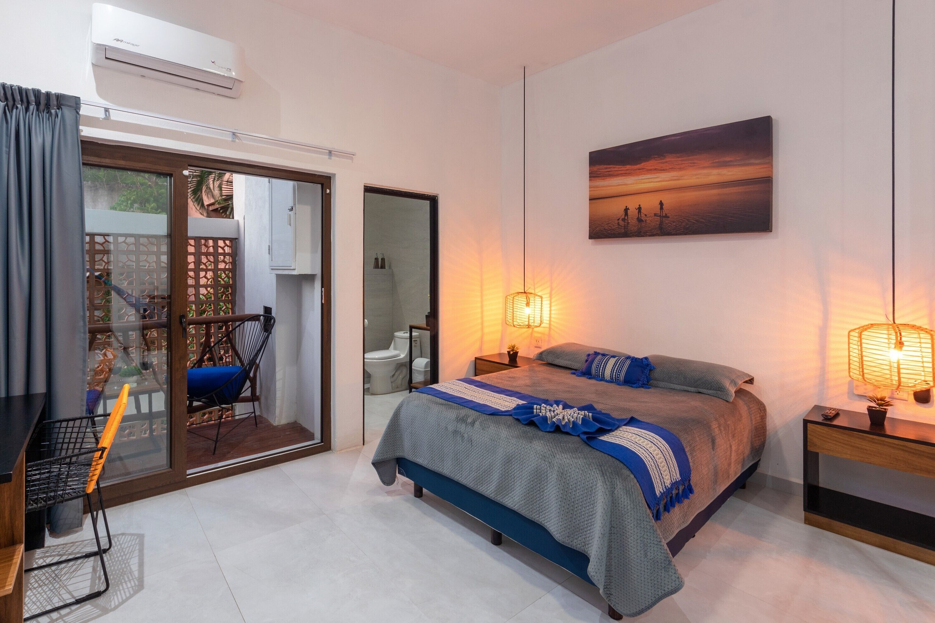 A bedroom with a bed, bedside lamps, a painting, and a view through a sliding door.
