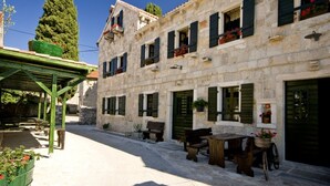 A stone building with multiple windows and shutters, outdoor seating, and a covered area with steps leading to a door. - Apartment in Sukošan with Balcony, Air condition, WIFI (4941-1) (Sukošan)