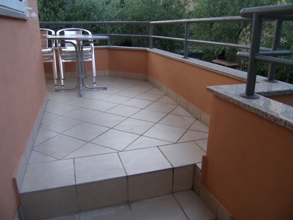 Un petit balcon extérieur doté d’un sol carrelé, de chaises en métal et d’une rambarde en métal.