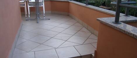 Un petit balcon extérieur doté d’un sol carrelé, de chaises en métal et d’une rambarde en métal.