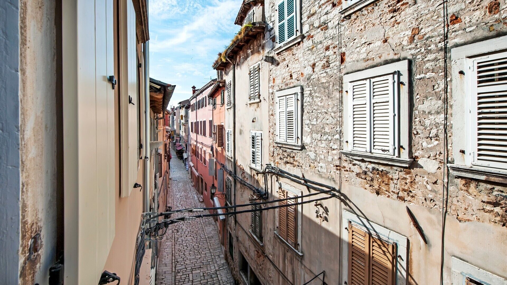 A narrow cobblestone street flanked by historic buildings with traditional shutters and balconies.