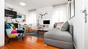 A modern living room with a grey sofa, colorful armchair, and a dining area with a table and chairs. - Studio Sunrise with Sea view (Rovinj)