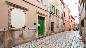 A narrow cobblestone street flanked by historic buildings with traditional architecture, including a green door and a white door with a black handle. - Studio Sunrise with Sea view (Rovinj)