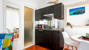 A compact kitchen with dark cabinetry, a stainless steel range hood, and a small dining area with a white chair and table. - Studio Sunrise with Sea view (Rovinj)