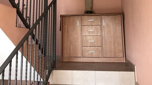Un escalier avec une rampe noire mène à un palier. Un meuble en bois, doté de tiroirs, est placé sur le palier.