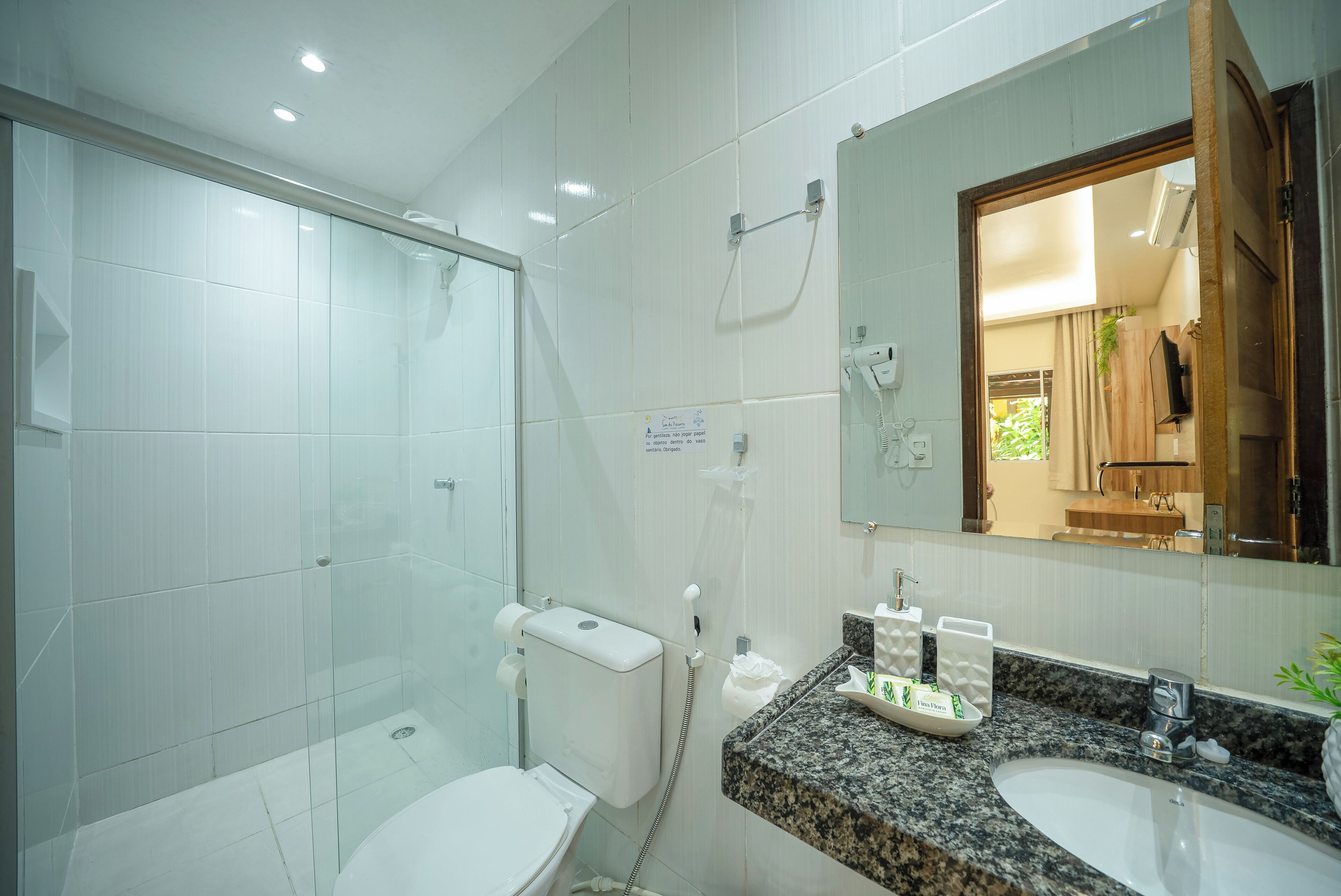 A bathroom with a glass shower enclosure, a toilet, a sink with a granite countertop, and a mirror.