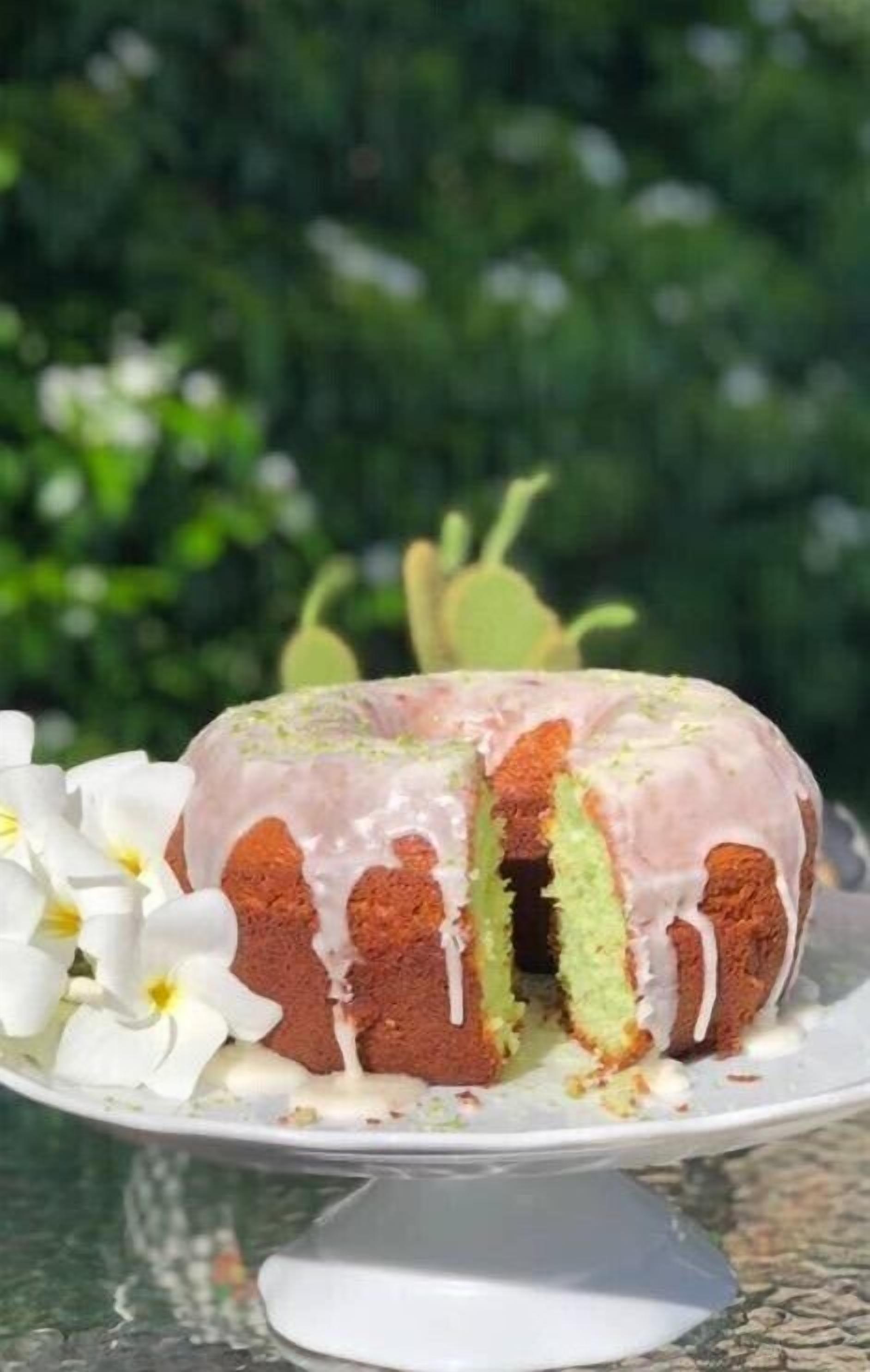 Un pastel con glaseado rosa sobre un plato blanco, rodeado de flores blancas.