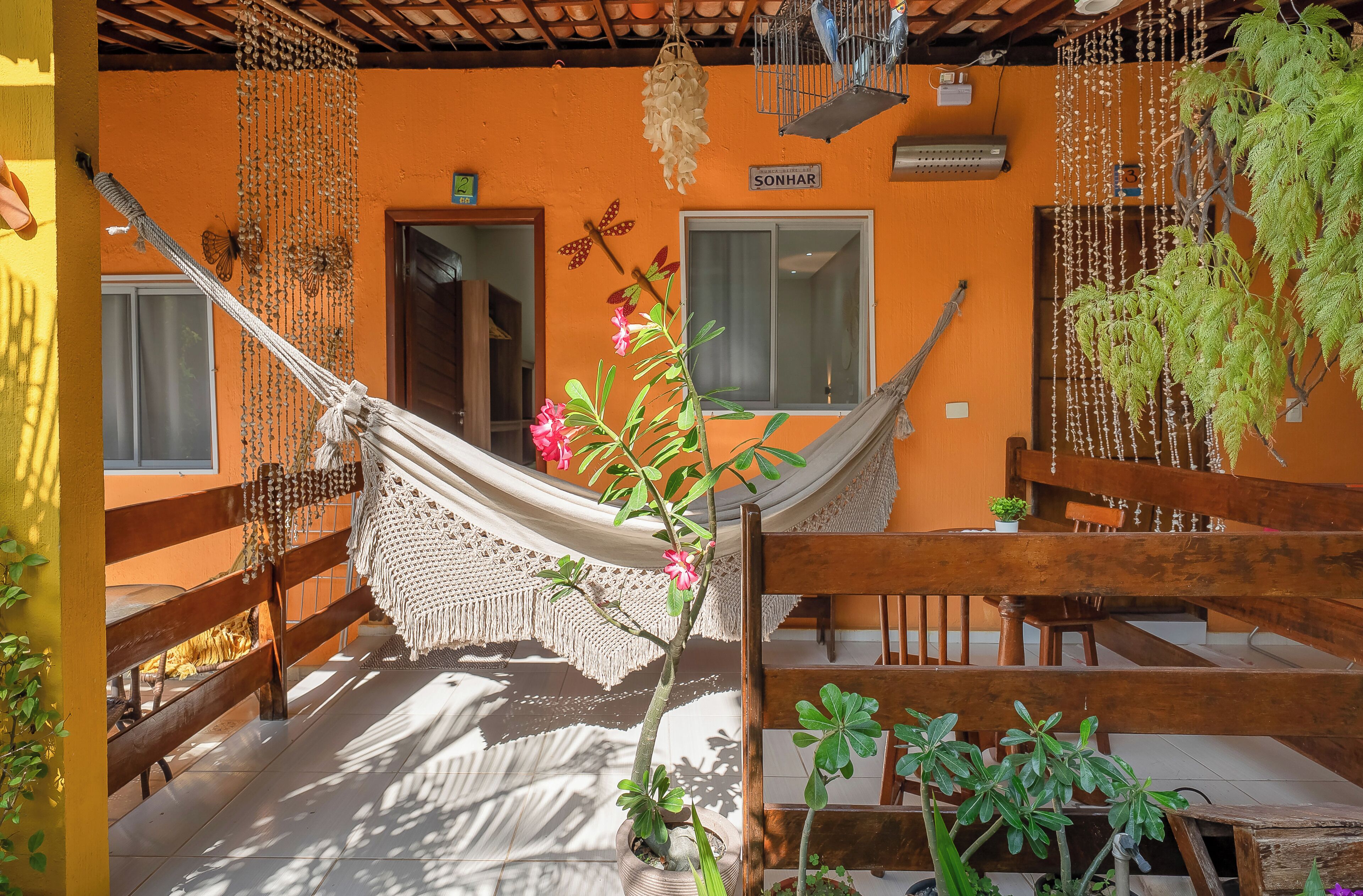 A hammock, wooden furniture, and potted plants in a room with orange walls and a wooden ceiling.