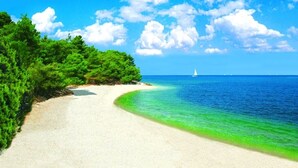 Una spiaggia con cielo sereno, un sentiero sabbioso e una barca a vela in lontananza.
