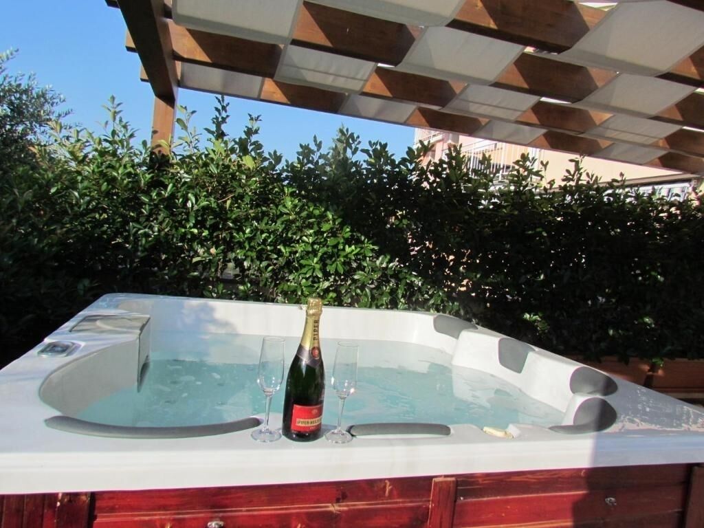 Un jacuzzi con una botella de champán y copas, rodeado de abundante vegetación.