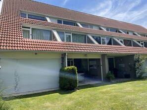 Une maison à deux étages, avec un toit recouvert de tuiles rouges, une véranda et un garage.