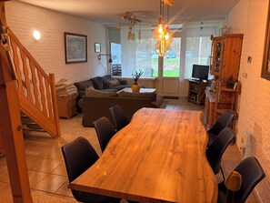 Un espace repas comprenant une table et des chaises en bois, un canapé et un escalier.