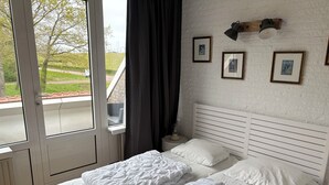 A bedroom with a bed, a window, and a wall-mounted lamp. - Cozy and friendly vacation apartment in a quiet location. (Bruinisse)