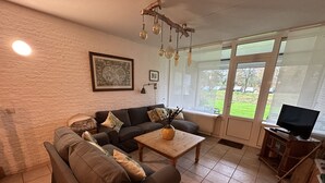 A living room with a sofa, a coffee table, a TV, and a window with a view of the outside. - Cozy and friendly vacation apartment in a quiet location. (Bruinisse)