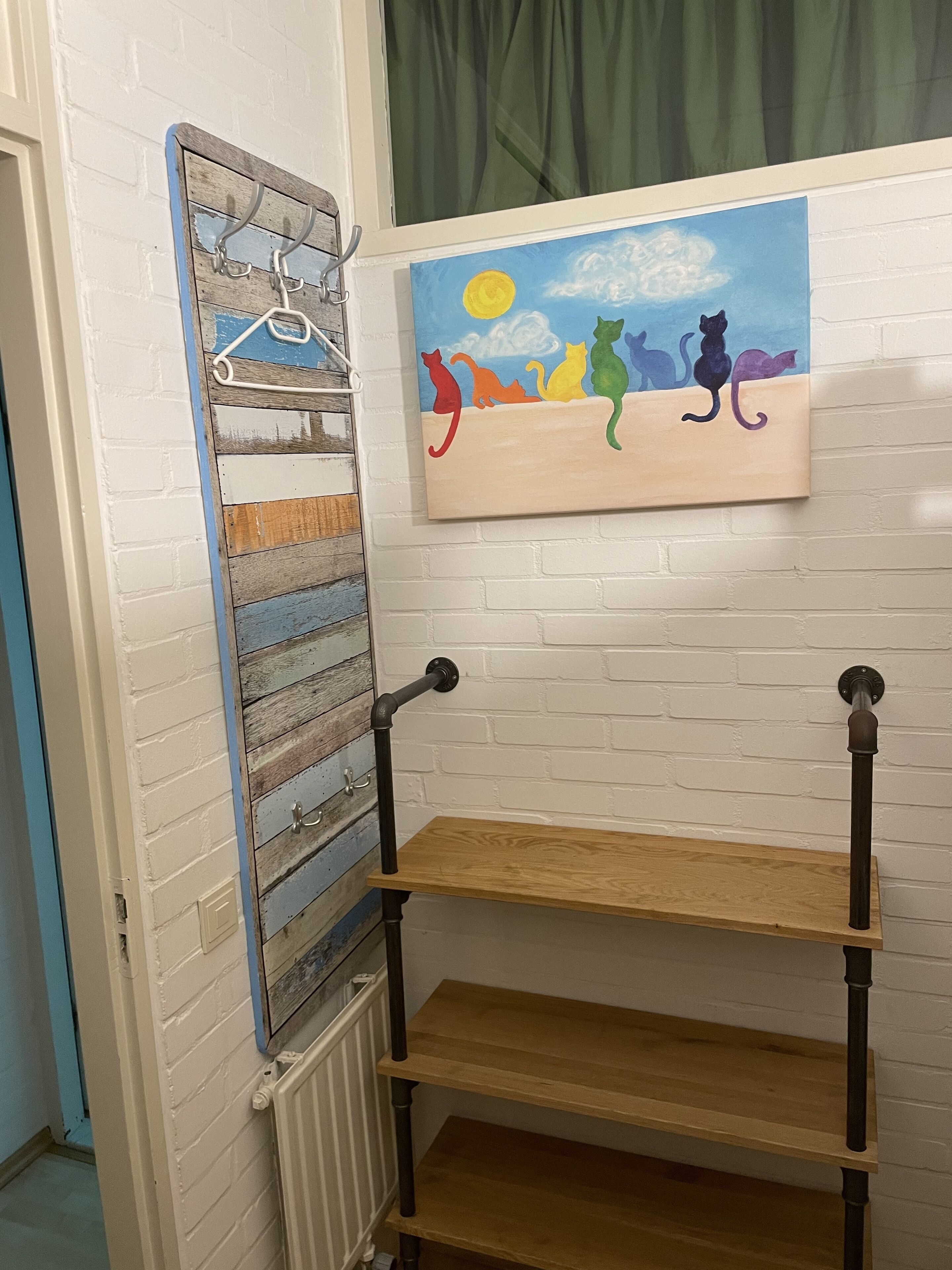 A room with a white brick wall, a wooden shelf unit with two shelves, and a painting of cats on the wall.