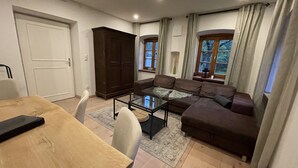 A living room with a brown sofa, a glass coffee table, a wooden dining table, and a dark wooden cabinet.