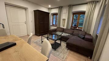 Ein Wohnzimmer mit einem braunen Sofa, einem Glastisch, einem Holzesstisch und einer dunklen Holzkommode.
