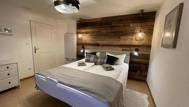 A bedroom with a wooden headboard, a bed with a grey blanket, two bedside lamps, and a white door.