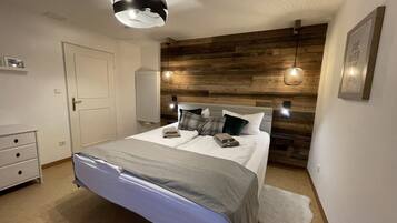 Ein Schlafzimmer mit einem hölzernen Kopfende, einem Bett mit grauer Decke, zwei Nachttischlampen und einer weißen Tür.