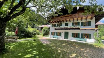 Un chalet traditionnel doté d’un toit en pente, de balcons en bois et d’un jardin agrémenté d’un banc et d’un parasol.