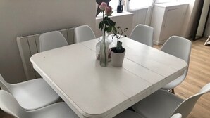 A white dining table with four chairs, a potted plant, and a vase with flowers. - Magnifique Maison de Ville Familiale (Courseulles-sur-Mer)