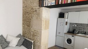 A compact living space with a sofa, a washing machine, and a kitchenette. - Magnifique Maison de Ville Familiale (Courseulles-sur-Mer)