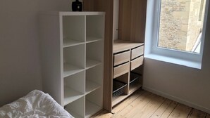 A bedroom with a large wardrobe, a window with a view of a stone wall, and a bed with a white duvet. - Magnifique Maison de Ville Familiale (Courseulles-sur-Mer)