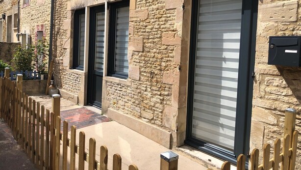 A stone building with a wooden fence, a large sliding door, and a small window. - Magnifique Maison de Ville Familiale (Courseulles-sur-Mer)
