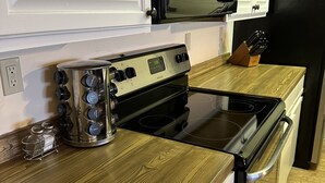 A kitchen with white cabinets, a stainless steel stove, a black microwave, and a wooden countertop. - Ski In Ski Out Condo (Whitefish)