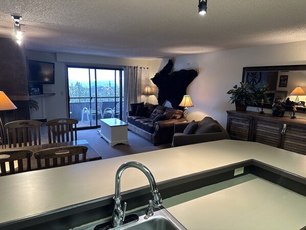 A modern kitchen with a central island, a dining area with chairs, a sofa, and a balcony with a view.