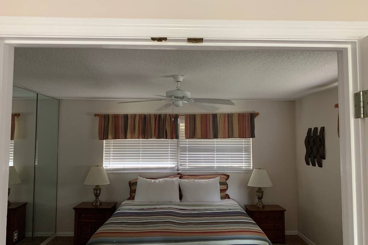 A bedroom with a bed, two bedside tables, a ceiling fan, and a window with blinds.