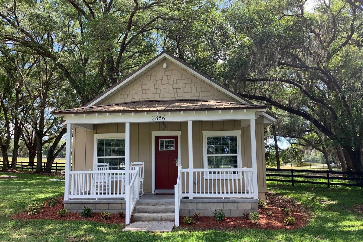 A small, single-story house with a red door, numbered 2886, featuring a front porch with white railings and a small front yard.