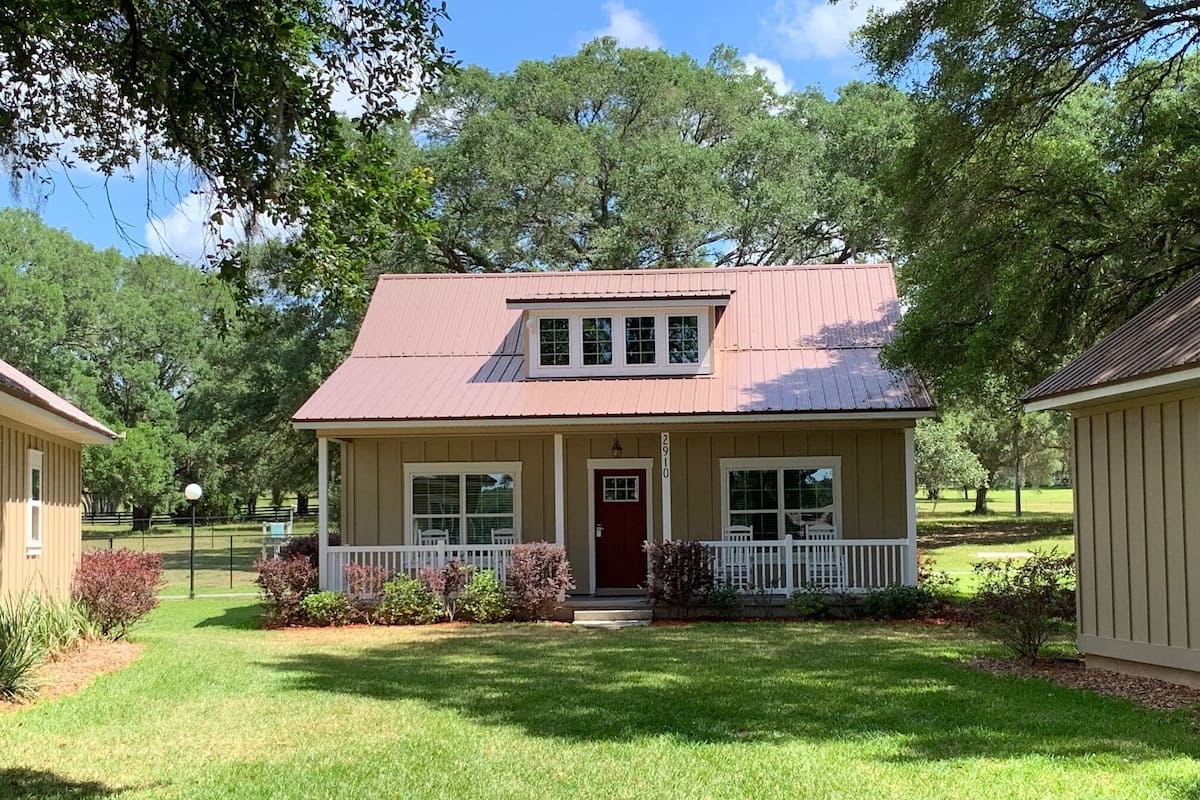A single-story house with a red door, white porch, and a small front yard.