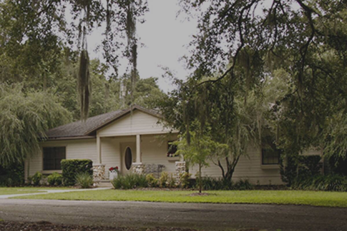 A single-story house with a front porch, surrounded by lush greenery and a small gazebo.