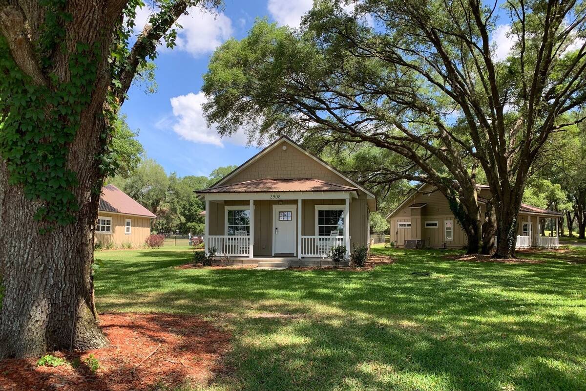 A single-story house with a front porch, a well-maintained lawn, and mature trees.