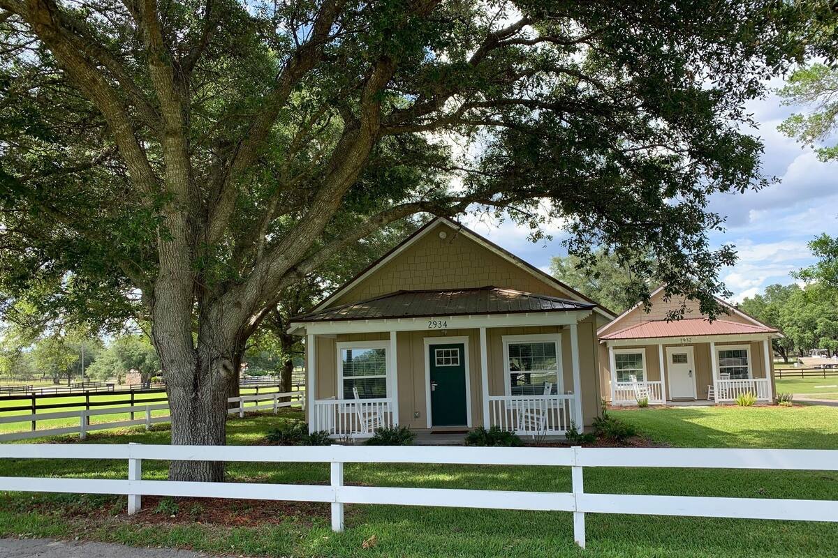 A two-story house with a porch, a green door, and a white fence in front.