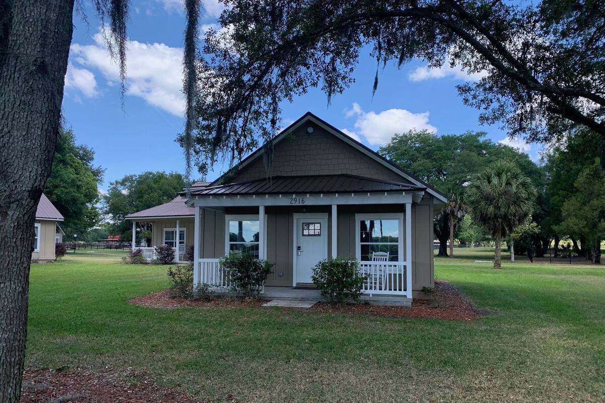 A small, single-story house with a porch, surrounded by a well-maintained lawn and trees.