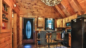 A wooden cabin interior with a dining area, kitchen, and a large chandelier.