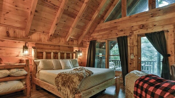 A wooden cabin bedroom with a bed, a chair, and a window.