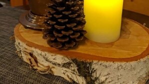 A candle on a wooden stand with a pine cone.