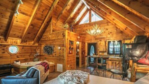 A log cabin interior with a loft bedroom, a dining area, and a kitchen.