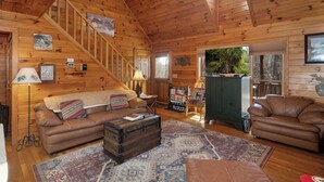 A cozy cabin interior with wooden walls, a staircase, a sofa, a coffee table, and a view of the outdoors. - Pet-Friendly,Cedar Cabin, Spa Tub, WiFi,Fireplace (Ferguson)